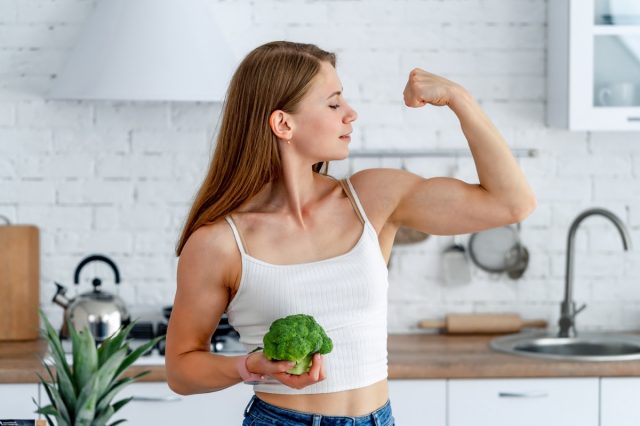Strong woman with broccoli in the kitchen