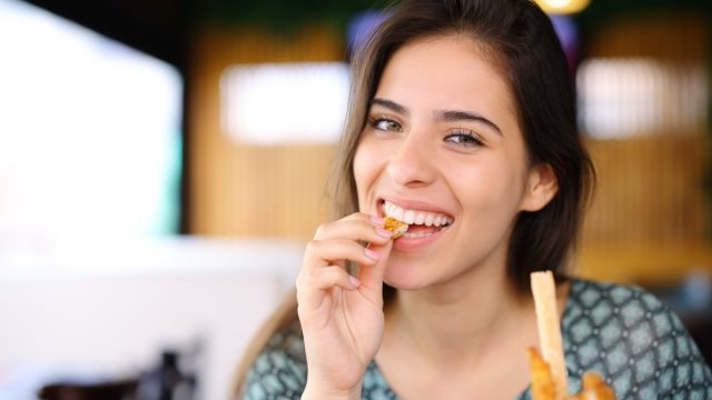 Happy woman eating chicken fingers looking at camera in a restaurant.