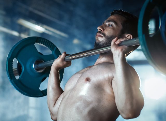 Close-up of a Muscular Shirtless Man Lifting Heavy Barbell and Doing Military Press Bodybuilding Exercise in the Industrial Gym Building.
