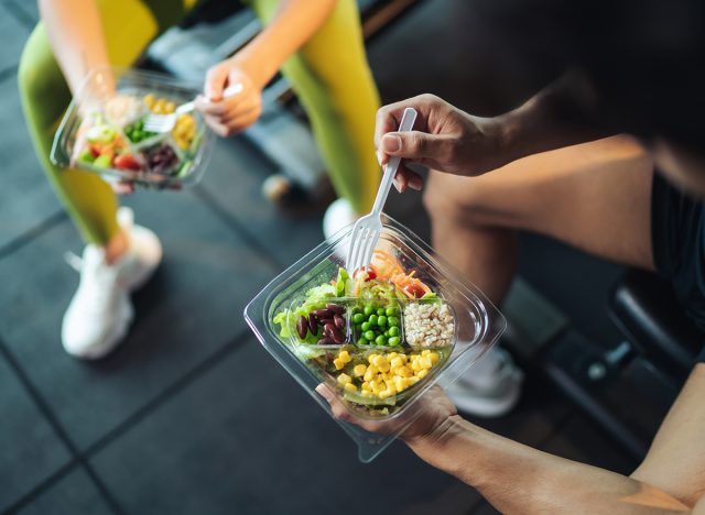Top view Asian man and woman healthy eating salad after exercise at fitness gym. Two athlete eating salad for health together. Selective focus on salad bowl on hand.