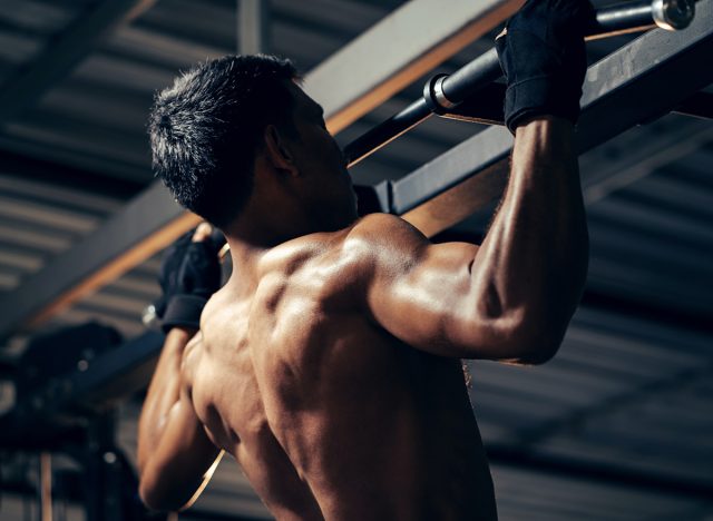Bodyweight workout. Athletic pulling up showing back muscle at gym. Muscular man exercise pull up on bar in fitness gym.