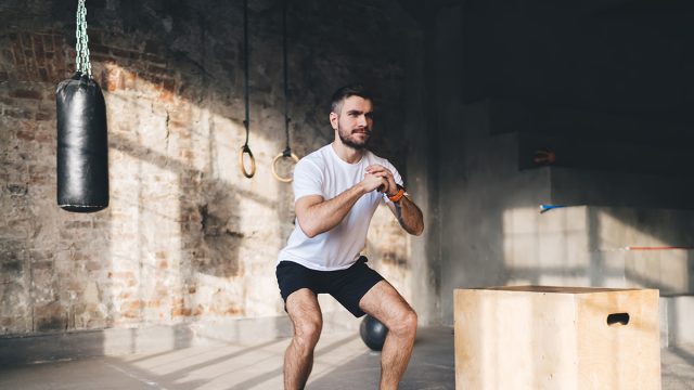 Full length of muscular man in sportswear doing squats during intense training at modern sports center with fitness equipment for workout