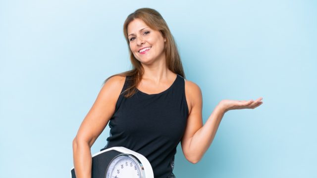 Middle aged,Caucasian,Woman,Isolated,On,Blue,Background,With,Weighing,Machine