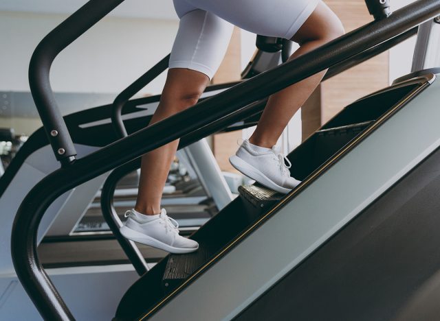 Cropped up photo shot young strong skinny sporty athletic sportswoman woman in white sportswear warm up train run on a treadmill climber stairs machine in gym indoor Workout sport motivation concept