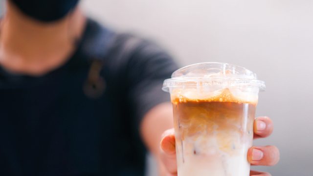 Cold brewed iced latte coffee, Ice coffee latte cup in a plastic glass on. barista hand in coffee cafe.banner background.Cold brew coffee ads.Latte with milk caffeine.plastic ice cup.Arabica roasted.