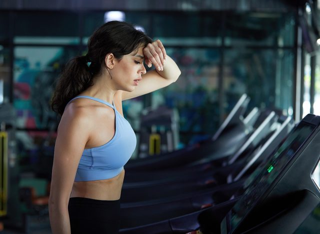young sports woman working out, running and feeling tired on treadmill in gym
