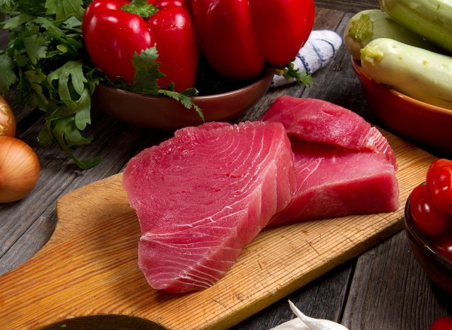 Raw tuna, onions, garlic, tomatoes, bell peppers, parsley and zucchini on a table