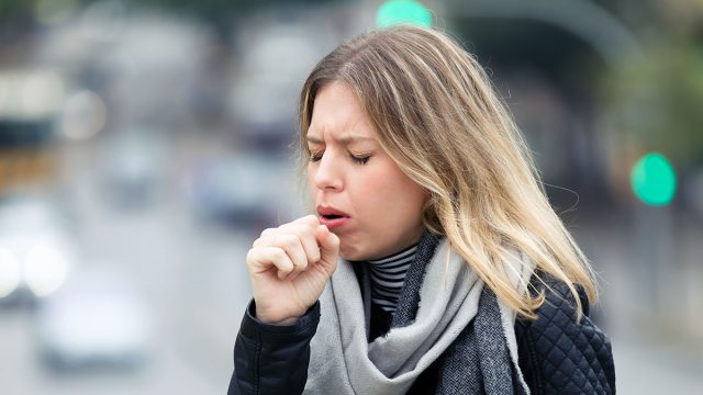 Shot of illness young woman coughing in the street.
