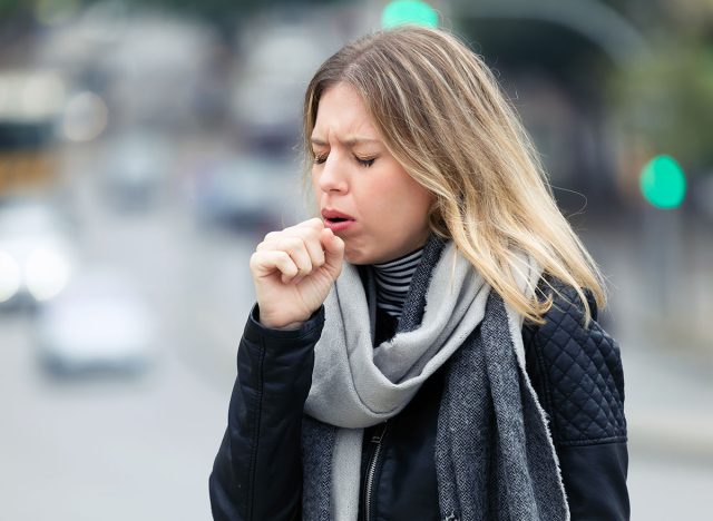 Shot of illness young woman coughing in the street.