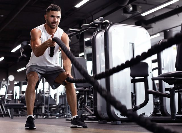 Athletic young man with battle rope doing exercise in functional training fitness gym.