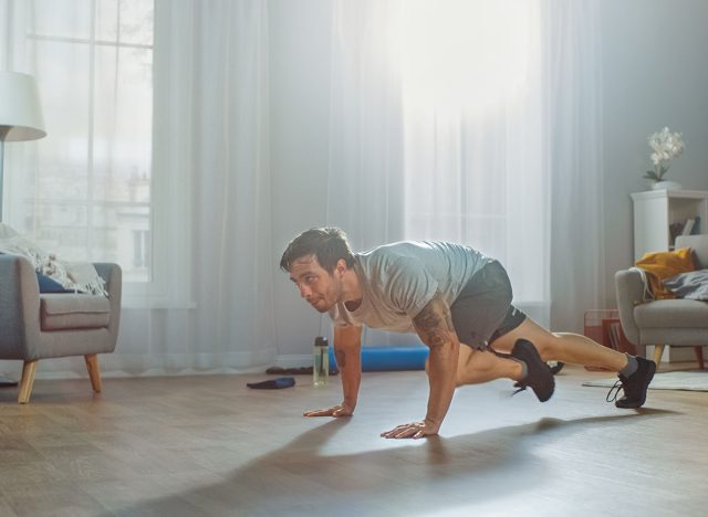 Muscular Athletic Fit Man in T-shirt and Shorts Energetically Starts Doing Mountain Climber Exercises at Home in His Spacious and Bright Apartment with Modern Interior.