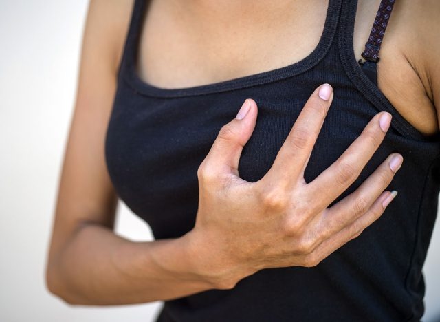 Closeup cropped portrait young woman with breast pain touching chest, selective focus