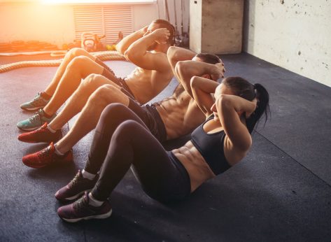 Group of athletic adult men and women performing sit up exercises to strengthen their core abdominal muscles at fitness training