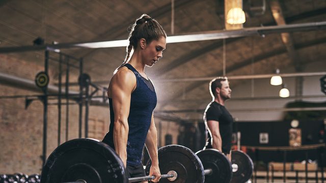 Strong woman and man holding heavy barbells in gym. Horizontal indoors shot