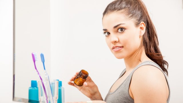 Woman holding a bottle of pills and vitamins to take in the morning in a bathroom