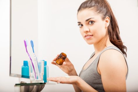 Woman holding a bottle of pills and vitamins to take in the morning in a bathroom