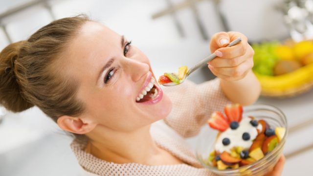 Happy young woman eating fruits salad.