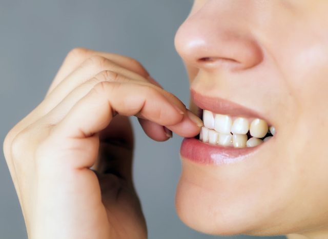nervous young woman biting her nails on gray background