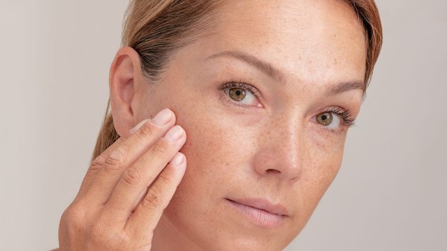 Portrait of cropped caucasian middle aged woman face with freckles touching skin by hand on white background