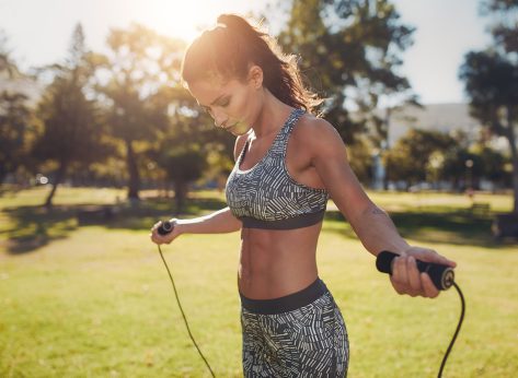 Portrait of fit young woman with jump rope in a park. Fitness female doing skipping workout outdoors on a sunny day.