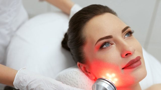 Facial Beauty Treatment. Woman Doing Red Led Light Therapy