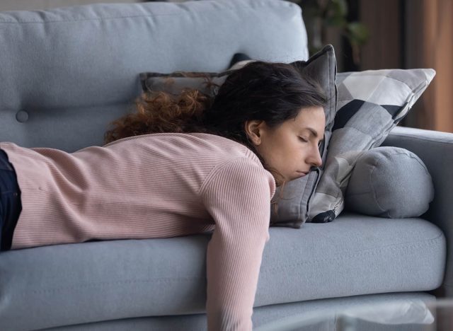Exhausted young Caucasian woman lying on comfortable sofa in living room sleeping after hard-working day, tired millennial female fall asleep on couch at home, take nap or daydream, fatigue concept