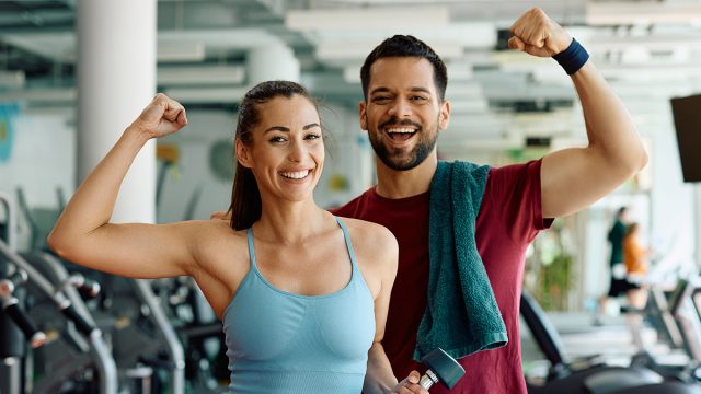 Happy athletic couple flexing their muscles after working out in a gym and looking at camera.