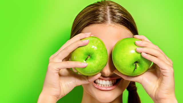 Funny,Laughing,Woman,Holding,Two,Gren,Apples,Before,Her,Eyes.