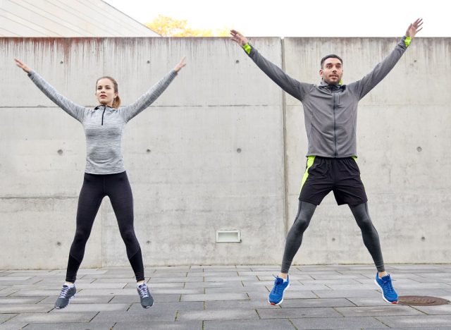 fitness, sport, people, exercising and lifestyle concept - happy man and woman doing jumping jack or star jump exercise outdoors