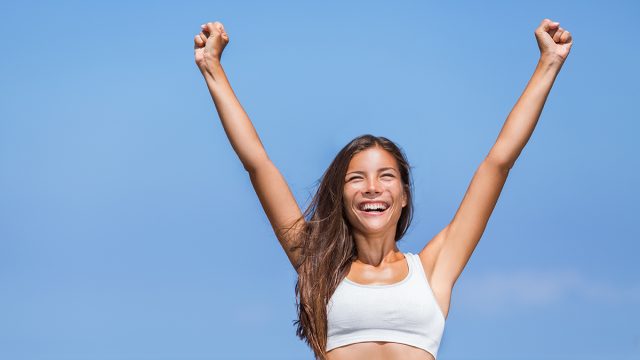 Happy fitness success woman winner. Asian girl cheering arms up of joy on summer beach.