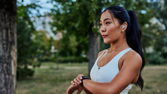Asian woman setting up the fitness smartwatch for running. Sportswoman checking watch device during workout in park