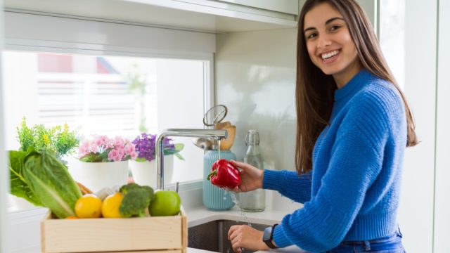 Young woman washing vegetables and fruit using water from sink