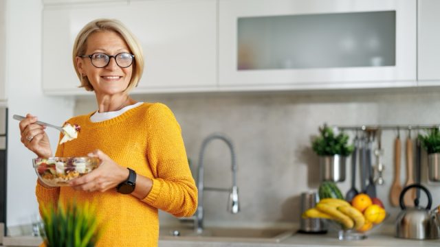 Mature woman eating salad at home.