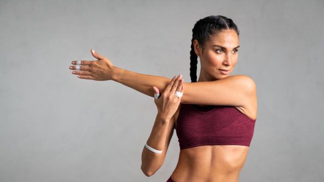 Portrait of fit middle aged woman doing arm stretching isolated on grey background