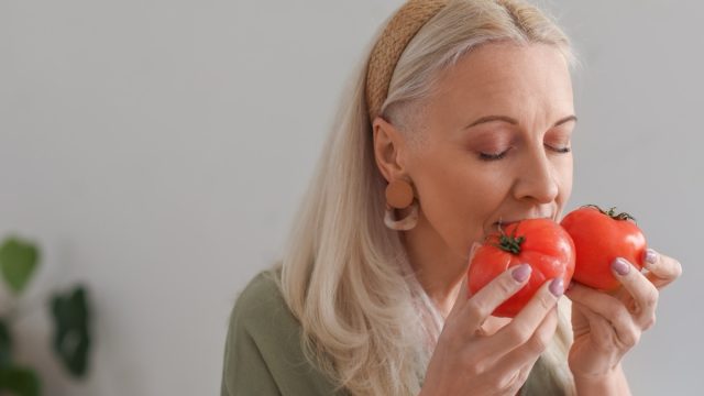 Mature woman with fresh tomatoes in kitchen, closeup.