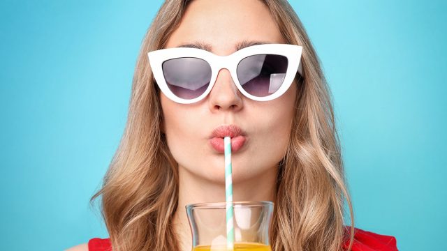 Beautiful woman drinks cocktail on blue background