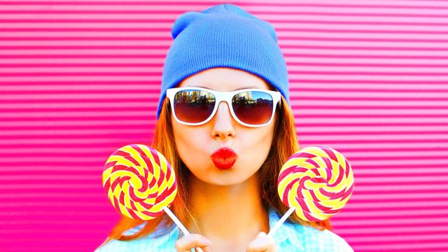 sweet woman holds two a lollipops is having fun on colorful pink background