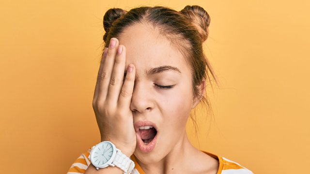 Beautiful brunette little girl wearing casual striped t shirt yawning tired covering half face, eye and mouth with hand. face hurts in pain.