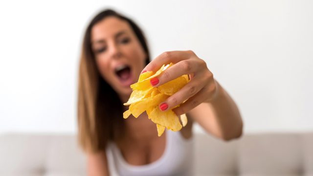 A young beautiful woman relaxing in comfortable cloth on the sofa at home having potato Chips.
