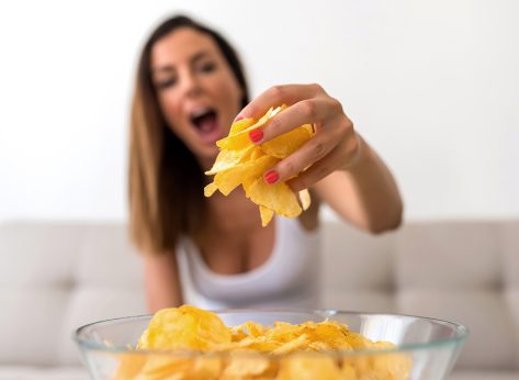 A young beautiful woman relaxing in comfortable cloth on the sofa at home having potato Chips.