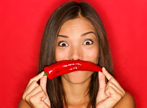 chili woman funny on red background holding red chili pepper vegetables as mustache looking funny at camera. Beautiful multicultural Caucasian / Chinese Asian girl on red background.