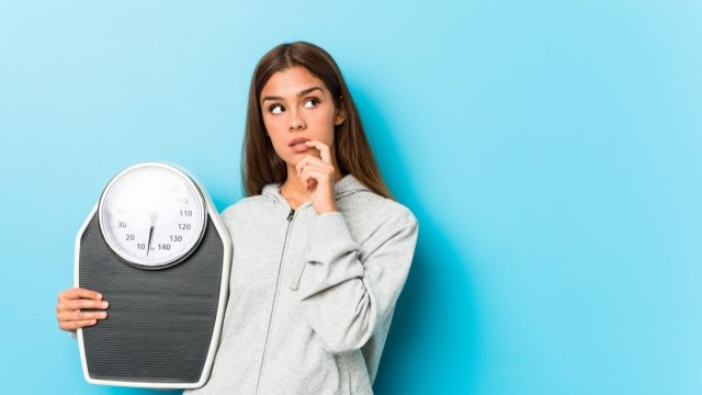 Young fitness woman holding a scale relaxed thinking.