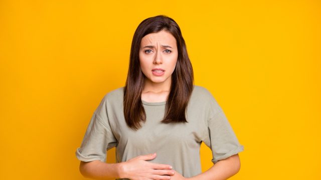 Portrait of pretty sick brown-haired girl touching abdomen.