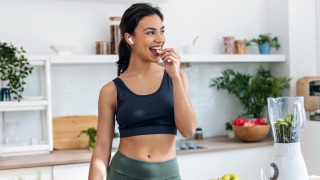 Shoot of athletic woman cutting fruits and vegetables to prepare a smoothie while listening to music with earphones in the kitchen at home.