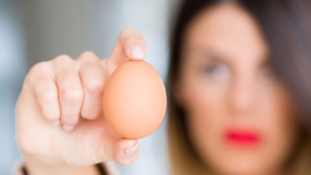Young beautiful woman holding fresh egg at home with angry face, negative sign showing dislike with thumbs down, rejection concept