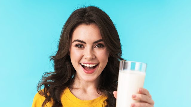 Image of happy positive optimistic young beautiful woman posing isolated over blue wall background holding milk.