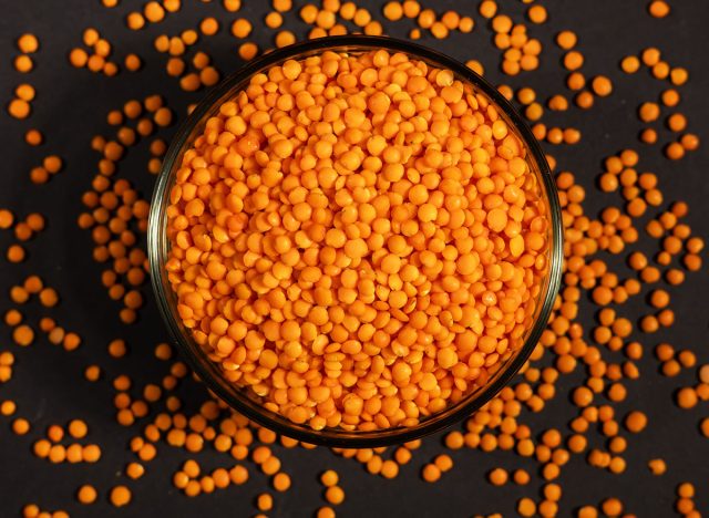 Red lentils in glass bowl. Dry orange lentil grains, heap of dal, raw daal, dhal, masoor, Lens culinaris or Lens esculenta on dark background