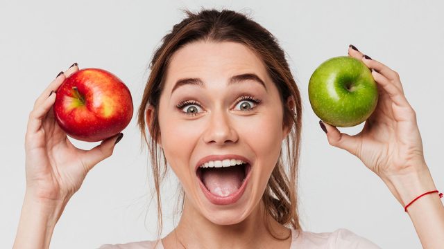 Portrait of a joyful happy girl holding apples and looking at camera isolated over white background