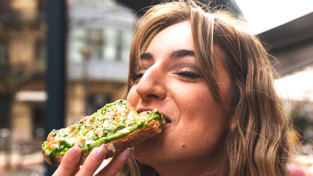 Young caucasian woman having breakfast at a terrace eating an avocado toast.