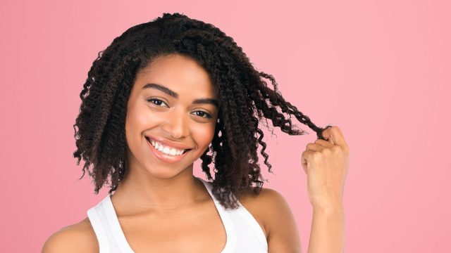 I Like You. Beautiful afro woman twirling hair, playing with her curls on a date, smiling at camera at studio, copyspace